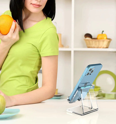 Woman in kitchen with Crystal Clear Acrylic Phone Stand For Desk holding iPhone, showcasing portability and lightweight design.