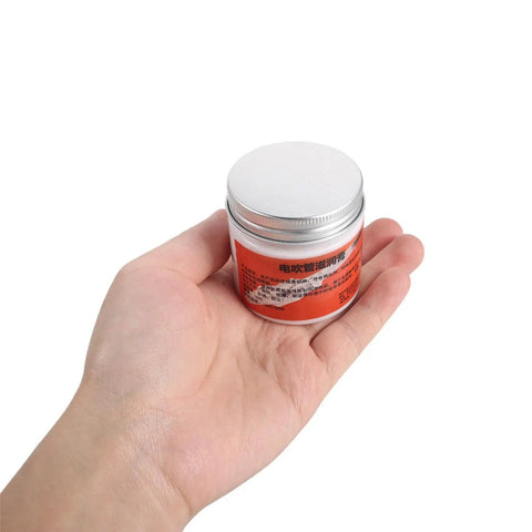 Hand holding a 3.53oz jar of All In One Conductive Grease for Electronics and Woodwinds, 3.53oz White Paste Delivers Stable Conductivity, Safe on Nickel, Brass, and Gold Connectors, Keeps Wind Instrument Switches Smooth and Refurbishes Worn Parts.