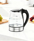 Electric Glass Kettle With Auto Shut Off 1.8L Borosilicate Glass Body Stainless Steel Inner Lid And Base No Plastic Touching Boiling Water Quick Boil Safe Pour Modern Countertop Tea And Coffee Kettle on a kitchen counter with fruits nearby.