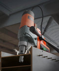 Angled front view of VEVOR magnetic drill press with orange/gray body, drilling into metal beam