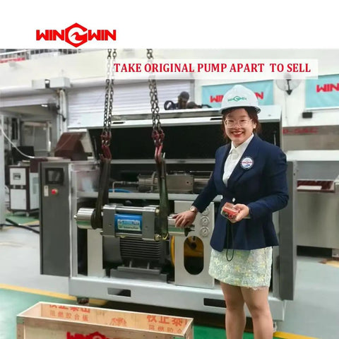 Person demonstrating industrial pump system in factory setting with overhead lifting equipment.