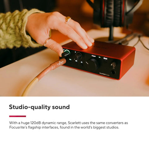 Hand adjusting Scarlett Solo Studio 4th Gen USB Audio Interface Bundle with dials and cables for recording, close-up view.