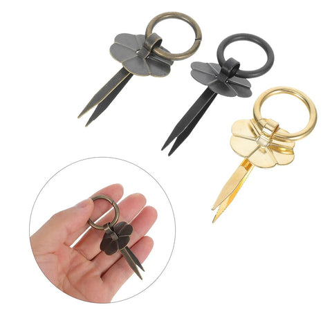 Three vintage round metal drawer pulls with integrated scissors design in gold and black, shown close-up in hand.