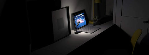 Clip On Book Light With 10 LED USB Rechargeable Reading Lamp illuminating a desk with a laptop, showcasing its portability and brightness modes.