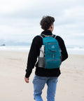 Person walking on the beach with Ultra Lightweight 20L Packable Daypack For Travel, Hiking And Camping, Foldable And Compact, teal color.