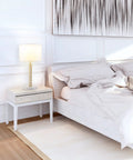 Paloma Table Lamp By Novogratz X Globe in bedroom, on nightstand with white bedding, modern glam cutout body and white fabric shade