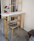 Rock Solid X Frame Steel Pipe Table Legs For Coffee Tables And Bars support a sleek white counter and golden chair in a modern setting.