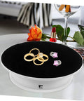 Rotating Electric Turntable Display Stand With Smooth Motorized Motion showcasing gold rings and earrings on a black surface.