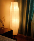 Foldable Rice Paper Floor Lamp Shade In Minimalist Modern Style next to a bed and nightstand in a softly lit bedroom, 43.3 cm tall.