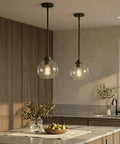 Straight Up Matte Black Globe Pendant Lights 2 Pack With Clear Glass Shades hanging above a kitchen island with natural decor.