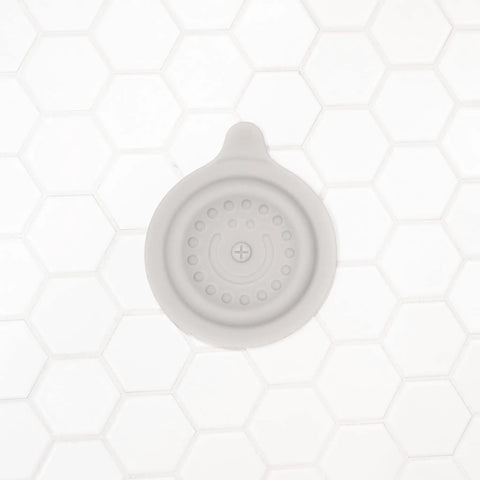 Premium Soft Silicone Bathtub Drain Stopper With Super Strong Suction Cup Locks Water In Fast For Baby Bath Times Easy Peel Grip Gray Tub Plug on white hexagon tiles.