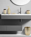 Golden Modern Small Trash Can Wastebasket For Bathrooms Powder Rooms Kitchens And Home Offices Durable Ceramic Round Garbage Container Bin Compact Space Saving Design That Fits Under Sinks Cabinets Or On Counters next to a sink in a modern bathroom.