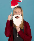 Person holding Santa hat and beard prop against blue background
