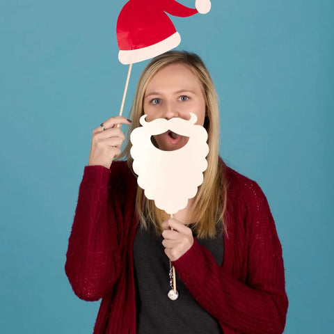 Person holding Santa hat and beard prop against blue background