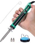 Hand holding desoldering soldering iron kit with solder sucker pump, showing shorter handle and tips next to nozzles and stand.