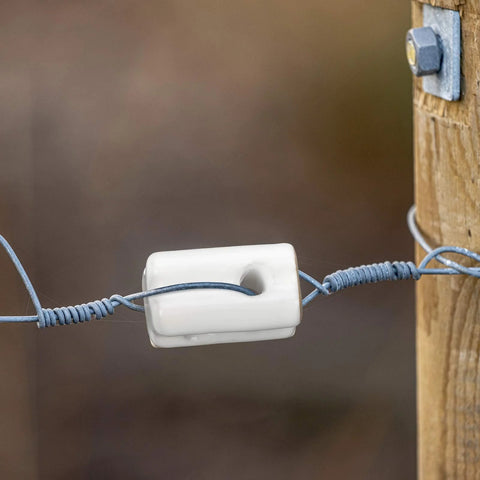 Porcelain bullnose fence insulator, white ceramic, on wire attached to a wooden post