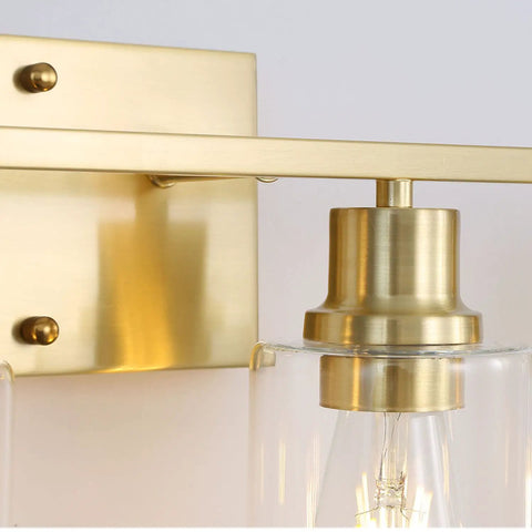 Close-up of the brushed brass fixture of a Three Light Sleek Gold Brushed Brass Vanity Light Fixture With Clear Glass Shade
