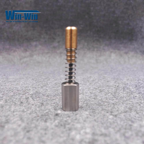 Electronic shift actuator assembly with brass top, coil spring, and gray base, front view.