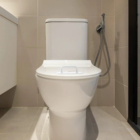 Front view of a toilet in a modern bathroom setting with beige tiles and a handheld bidet sprayer visible on the side.