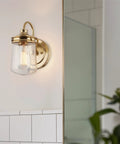Brass wall sconce with clear glass shade on tiled bathroom wall
