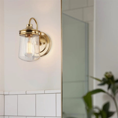 Brass wall sconce with clear glass shade on tiled bathroom wall