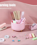 Pink Desk Accessories Set With Rotating Pen Holder, Stapler, Tape Dispenser, and Clips on a pink background