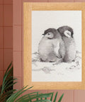 Framed watercolor painting of two penguin chicks on a pink tiled wall background