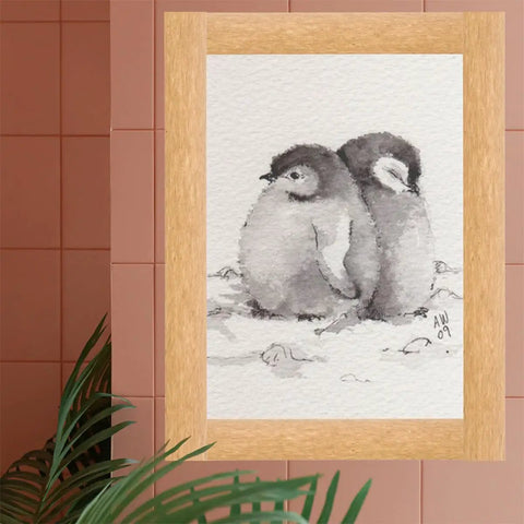 Framed watercolor painting of two penguin chicks on a pink tiled wall background