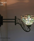 Tiffany Style Wall Sconce Plug In Swing Arm Light With Sea Blue Stained Glass Dragonfly Motif, lit at night on wall.