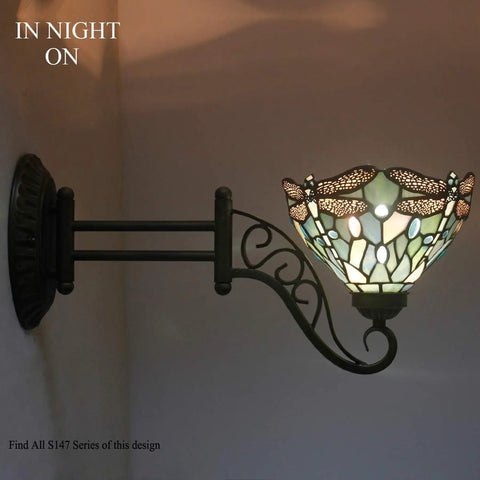 Tiffany Style Wall Sconce Plug In Swing Arm Light With Sea Blue Stained Glass Dragonfly Motif, lit at night on wall.