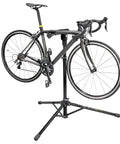 Elite Bike Repair Stand With Built In Parts Bin Stable Tripod Design 360 Degree Rotating Clamp Head Non Marking Rubber Jaws For A Secure Hold Easy Fold Travel Ready Pro Grade Stand For Quick At Home Or Shop Tune Ups holding a bike