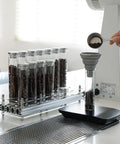 Single Dose Coffee Bean Storage Tubes, Glass And Aluminum Vials, Fourteen Piece Set With Acrylic Board on kitchen counter.