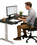 Fly One Touch Electric Rising Desk For Home Office And Gaming Dope Ergonomic Sit Stand Workstation With Silent Motor Smooth Height Adjustments Gotta Keep It Comfy All Day Long, man working on a computer at a sturdy height-adjustable desk.