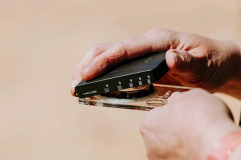 Hands holding Advanced Mirror Compass For Pros And Serious Hikers With Metric UTM Scales And Inch Ruler.