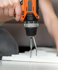 Person using orange and black power drill with a screwdriver bit on a white surface