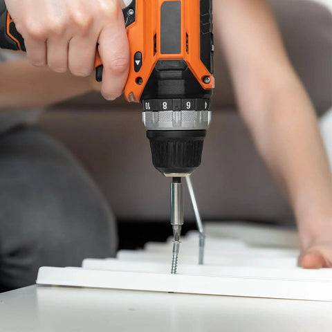Person using orange and black power drill with a screwdriver bit on a white surface