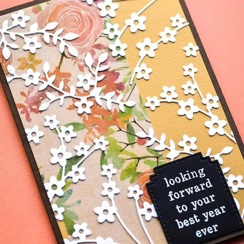 Handmade card with floral paper, die cut white flowers, and black tag reading 'looking forward to your best year ever'