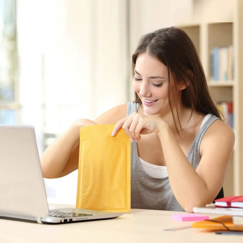 Person using 50 Pack Bubble Mailers 4x8 Inches Self Seal Kraft Poly Padded Envelopes With 80gsm Bubble Lining For Lightweight Shipping Bags Ideal For Small Biz For All Online Sellers next to laptop.