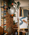 Artist uses lightweight studio lamp with foldable tripod and adjustable aluminum shade for painting on canvas indoors.