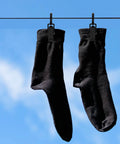 Black socks hanging on a line with rotatable plastic curtain clips with swivel hooks against a blue sky.
