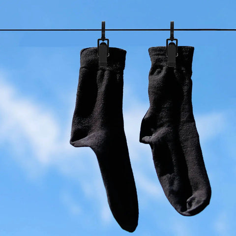 Black socks hanging on a line with rotatable plastic curtain clips with swivel hooks against a blue sky.