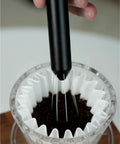 No Fuss WDT Needle Tool For Espresso Brewing retractable stirrer in use over coffee grounds in a filter.