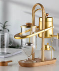 Top Shelf Belgian Siphon Coffee Maker With Stunning Gold Finish Built From Heavy Glass And Steel Frame Relies On Steam Heat And Gravity Action To Pull Silky Smooth Brews Fast Sick Flex For True Coffee Geeks Wanting Elite Taste At Home Or Work - Manual brewer with gold and glass design.