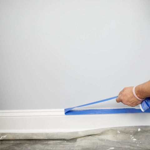 Applying ProGrade Painter Tape With PaintBlock Technology Blue 1.5 Inch Wide Multi Surface Masking Tape along a white baseboard