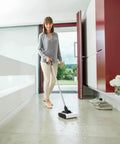 Woman using Cordless Electric Floor Sweeper Broom With Whisper Quiet Rollers For Hardwood Vinyl Tile And Rugs Lightweight Automatic Sweeper Machine For Pet Fur Hair Dust And Household Mess White on smooth floor.
