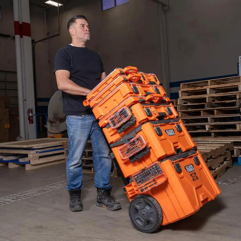 Person moving stacked orange toolboxes with wheels in a warehouse setting
