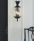 Three Light Outdoor Wall Mount Sconce In Matte Black With Pineapple Cut Glass mounted on white porch wall next to black door.