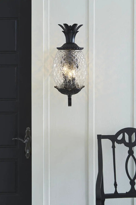 Three Light Outdoor Wall Mount Sconce In Matte Black With Pineapple Cut Glass mounted on white porch wall next to black door.