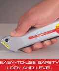 Hand holding Hidden Edge Utility Knife with Easy Safety Lock and Level, highlighting retractable blade and aluminum case in silver.