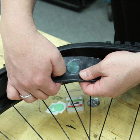 Hands applying patch from Bike Tire Patch Kit With Peel And Stick Patches And Extra Tough Tire Levers, Built In Sealant Inner Tubes